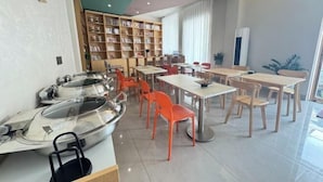 Un comedor moderno con varias mesas y sillas, una amplia estantería y una barra con equipo de cocina.
