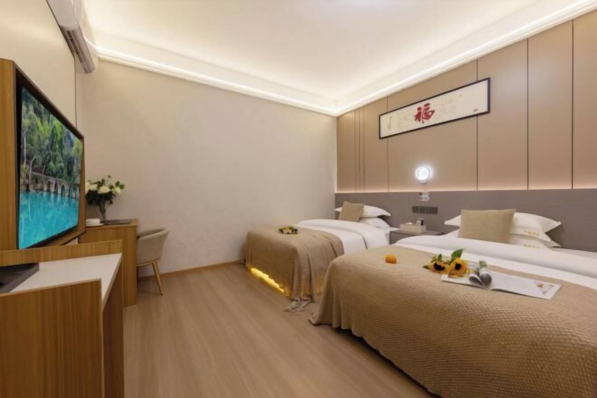 A hotel room with two beds, a desk, a TV, and a painting on the wall.