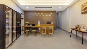 Zona de recepción con un escritorio de madera, dos taburetes altos, una máquina de café y una pequeña mesa con objetos encima.