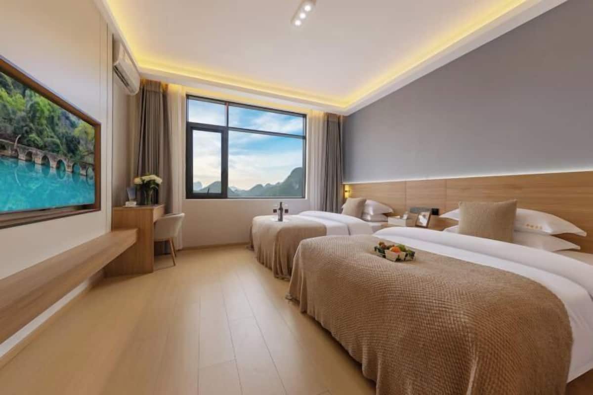 A hotel room with a large window, a desk, two beds, and a TV on the wall.
