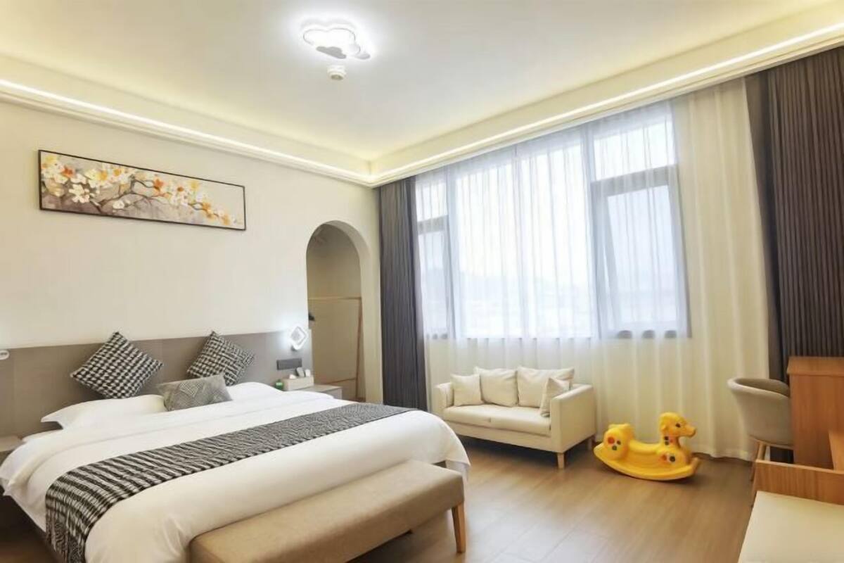 A hotel room with a bed, a sofa, a rocking horse, and a painting on the wall.