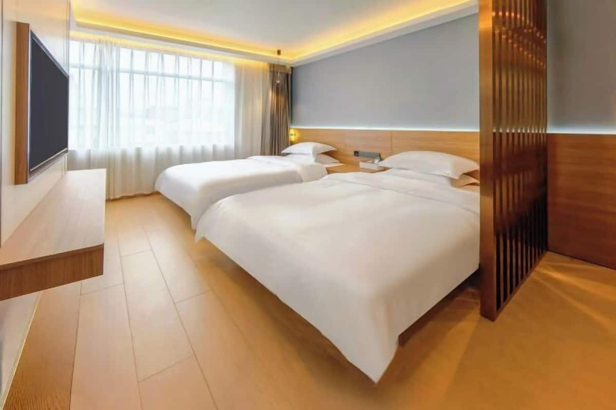 A hotel room with two beds, a TV, and a large window with curtains.