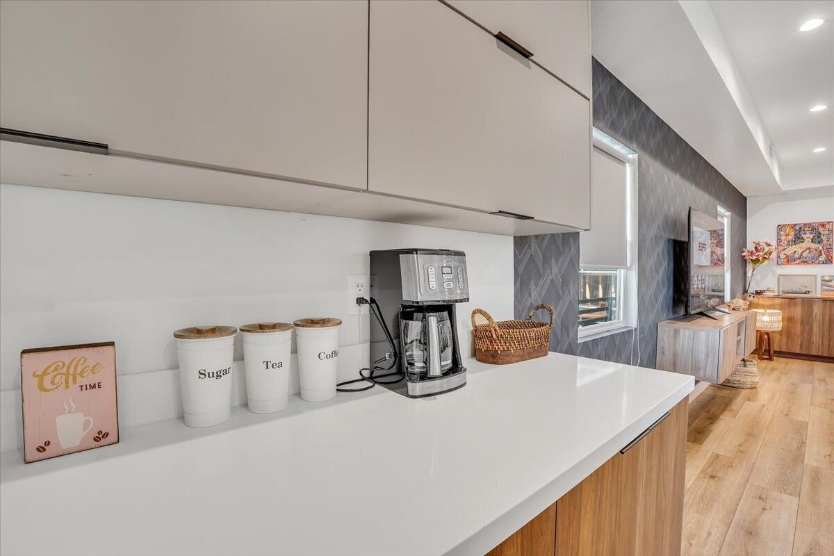 A modern kitchen with a white countertop, coffee maker, sugar and tea containers, and a basket.