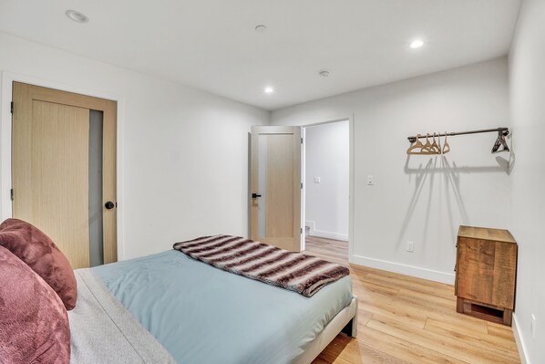 Un dormitorio con una cama, una puerta de madera, un perchero y un pequeño mueble de madera.
