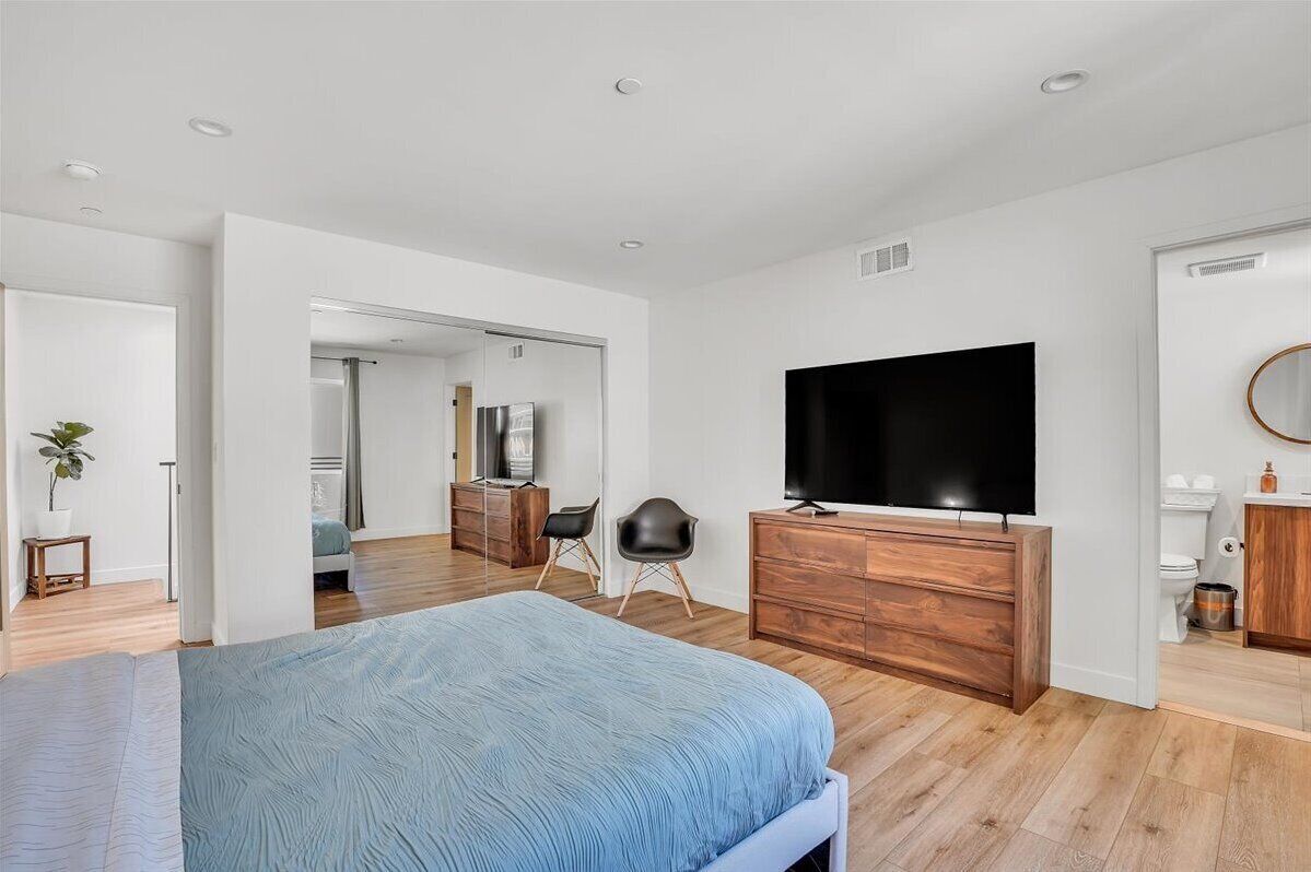 Un dormitorio moderno con una cama grande, un televisor y un aparador de madera.