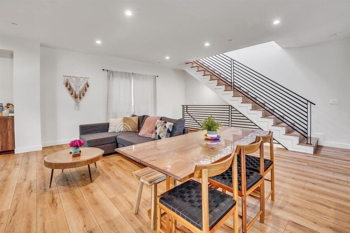 A modern living room with a wooden dining table, a sofa, and a staircase.