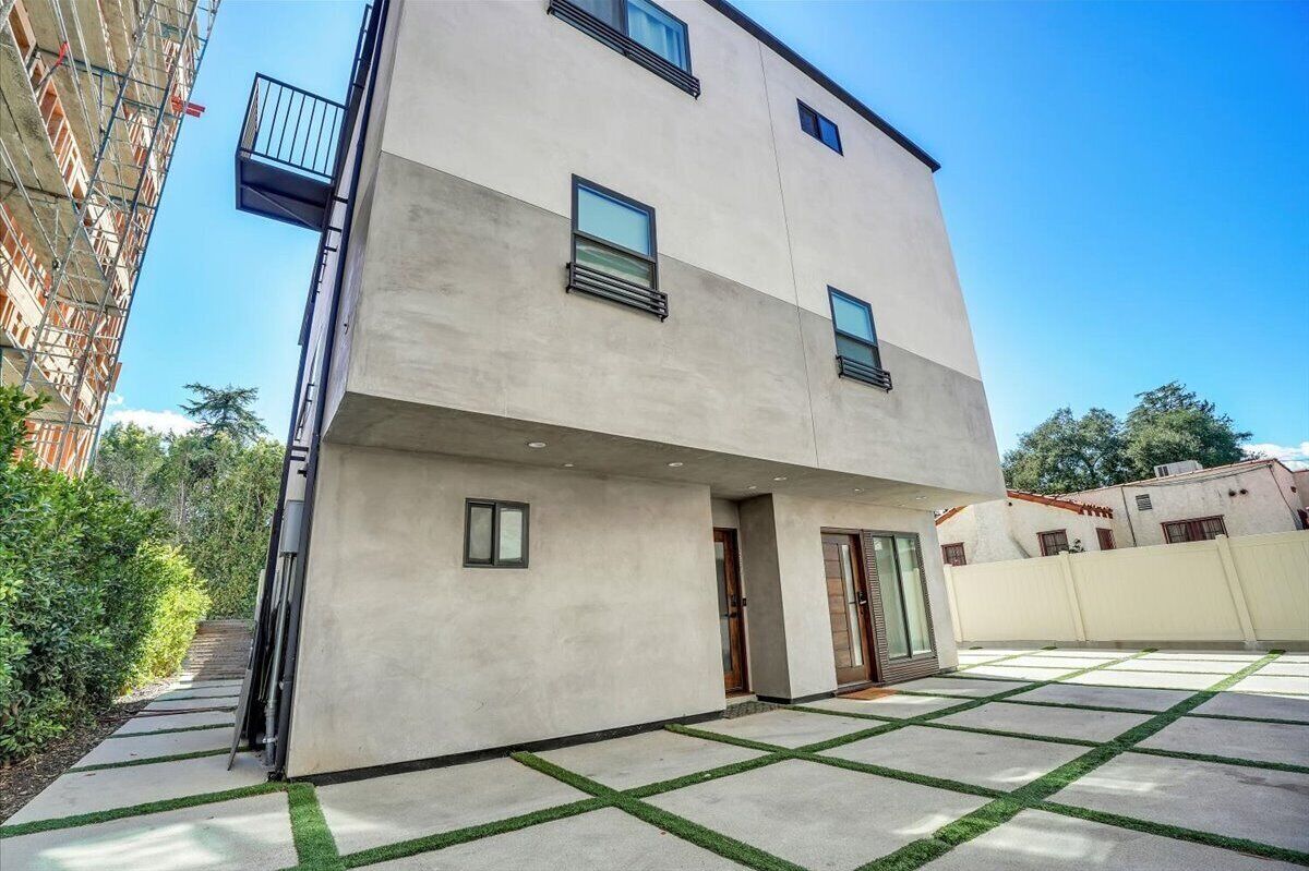 A modern two-story building with a flat roof, large windows, and a courtyard with artificial grass.