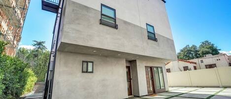 A modern two-story building with a flat roof, large windows, and a courtyard with artificial grass.
