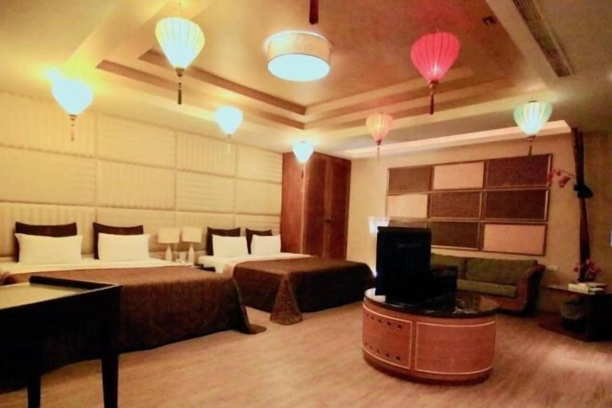 Een hotelkamer met een bed, nachtkastjes, een televisie, een bank en decoratieve hanglampen.