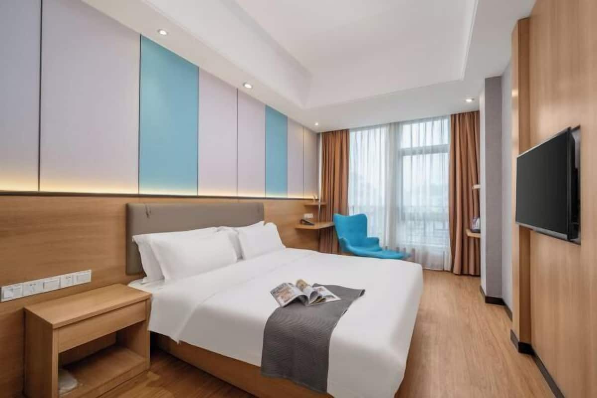 Ein modernes Hotelzimmer mit einem großen Bett, einem Nachttisch, einem Fernseher und einem Fenster mit Vorhängen.