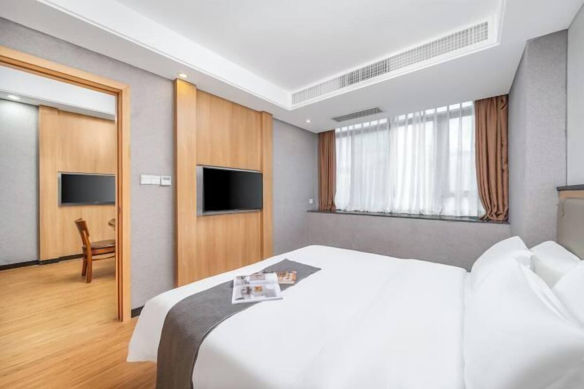 Ein Hotelzimmer mit Bett, Fernseher, Fenster mit Vorhängen und Tür.