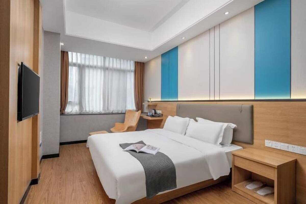Ein modernes Hotelzimmer mit einem großen Bett, einem Flachbildfernseher, einem Nachttisch und einem Fenster mit Vorhängen.
