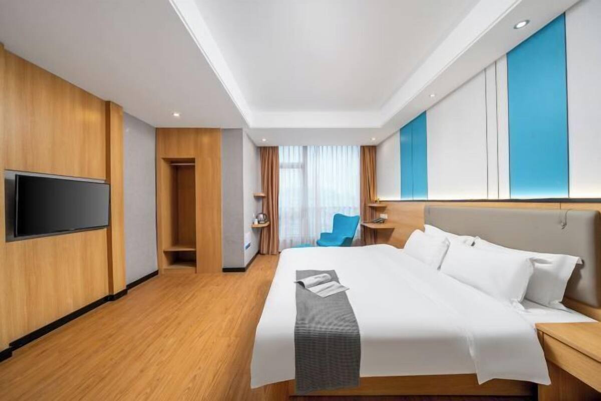 Ein Hotelzimmer mit einem großen Bett, einem an der Wand montierten Fernseher, einem Schreibtisch und einem Stuhl.
