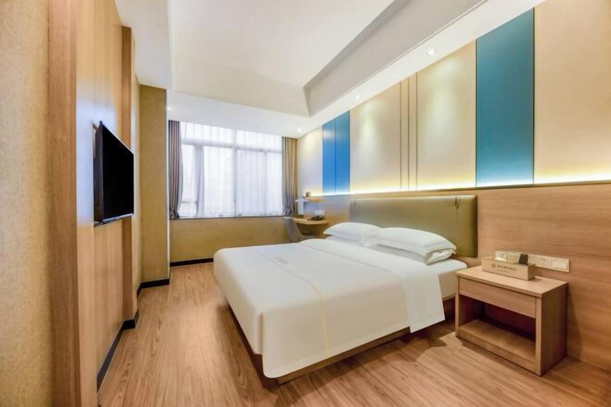 Ein Hotelzimmer mit Bett, Nachttisch und einem an der Wand befestigten Fernseher.