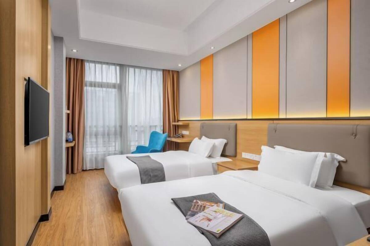 Ein Hotelzimmer mit zwei Betten, einem Fernseher, einem Schreibtisch und einem Fenster mit Vorhängen.
