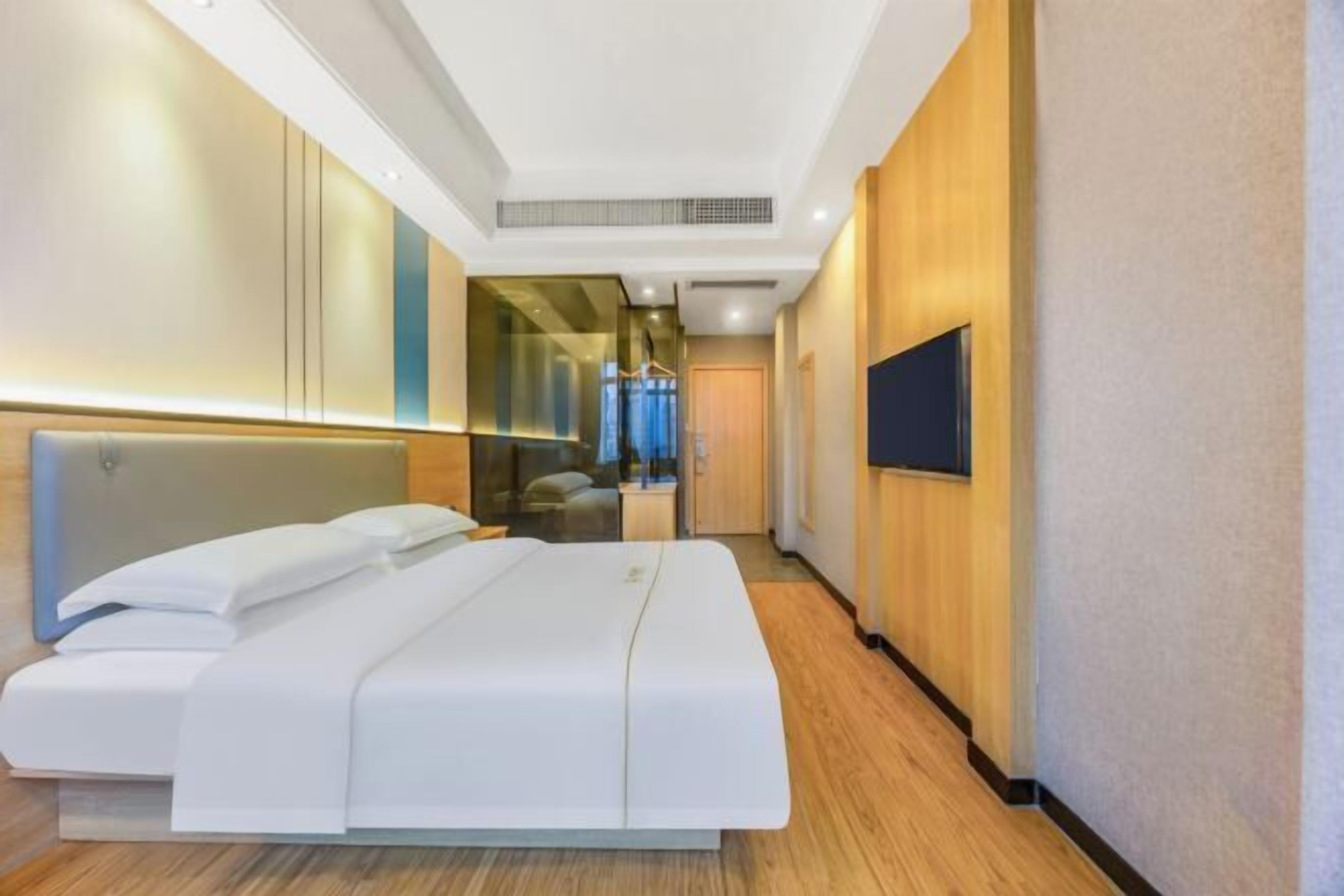 Une chambre d’hôtel moderne dotée d’un grand lit, d’un téléviseur à écran plat et donnant sur le couloir.