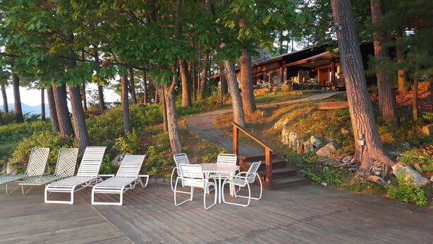 Une terrasse en bois avec des sièges extérieurs, entourée d’arbres et d’un bâtiment en pierre.