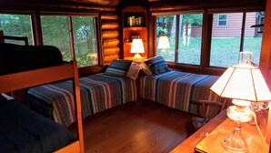Une chambre chaleureuse dans un chalet, avec deux lits superposés, une table en bois avec une lampe et une bibliothèque.
