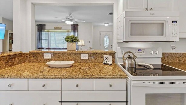 A modern kitchen with granite countertops, white cabinetry, a stainless steel kettle, and a microwave. - Dolphin Sands Retreat (Venice)