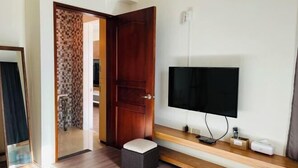 A room with a wooden door, a television mounted on the wall, a small stool, and a wooden shelf with electronic devices. - Taitung Yipin Garden Bed and Breakfast (Taitung)