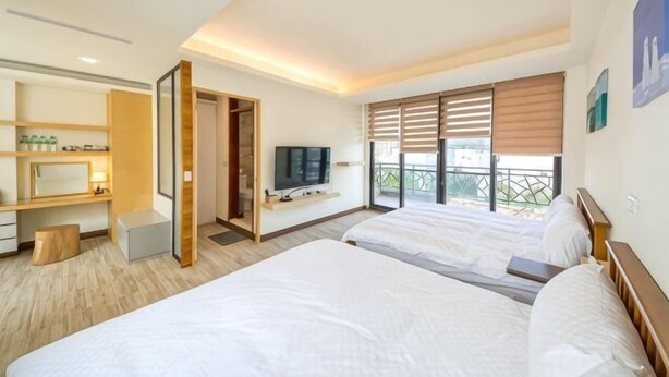 A hotel room with two beds, a TV, a desk with a chair, and a balcony with a view. - Taitung Yipin Garden Bed and Breakfast (Taitung)