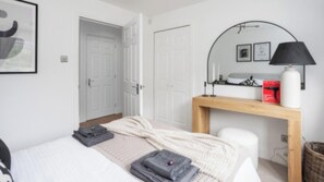 A hotel room with a bed, a bedside table with a lamp, a mirror, and a door leading to another room. - City Centre Apartment with 2 Private Car Spaces (Edinburgh)