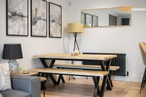 A modern living room with a wooden dining table, benches, a sofa, a lamp, and abstract wall art.