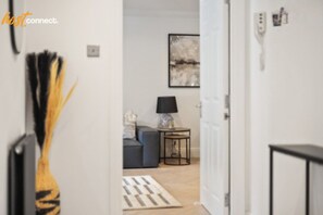 A hallway leading to a living room with a sofa, a lamp, and a framed artwork on the wall.