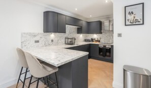 A modern kitchen with dark cabinetry, a marble countertop, and a bar area with stools. - City Centre Apartment with 2 Private Car Spaces (Edinburgh)