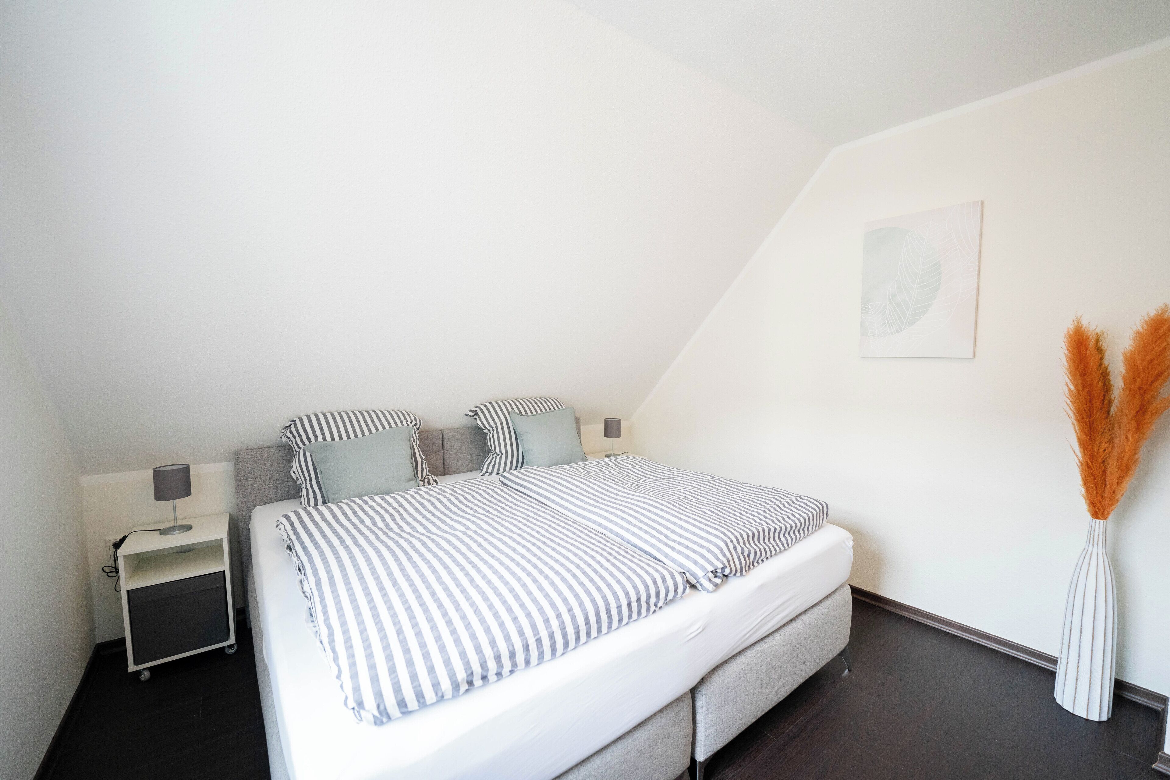 A neatly arranged bedroom with a bed, bedside tables, and a wall-mounted artwork.