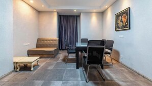 A small, well-lit room with a sofa, a dining table with chairs, and a painting on the wall.
