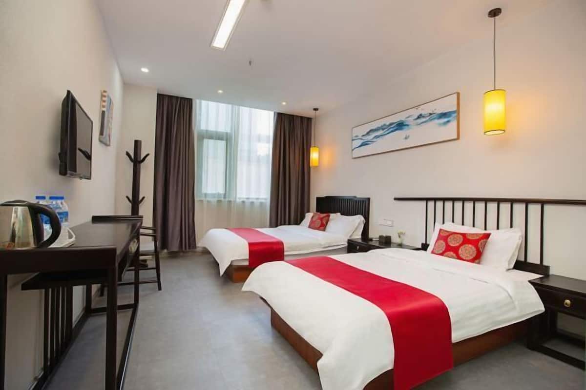 Une chambre d’hôtel avec deux lits, un bureau, une chaise, une télévision et une fenêtre avec des rideaux.