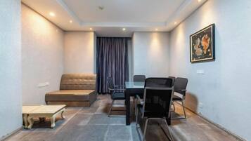 A room with a sofa, a dining table with chairs, a small table, and a painting on the wall.