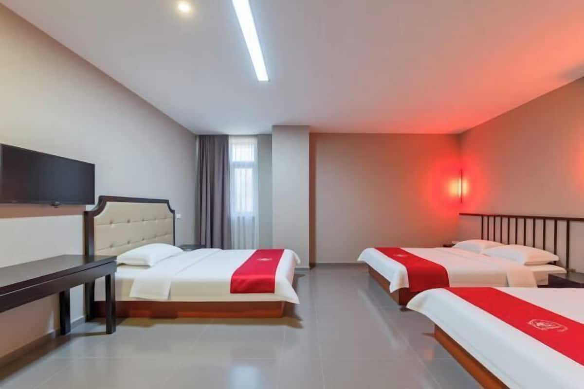 Une chambre d’hôtel avec deux lits, un banc, une télévision et un lampadaire rouge fixé au mur.
