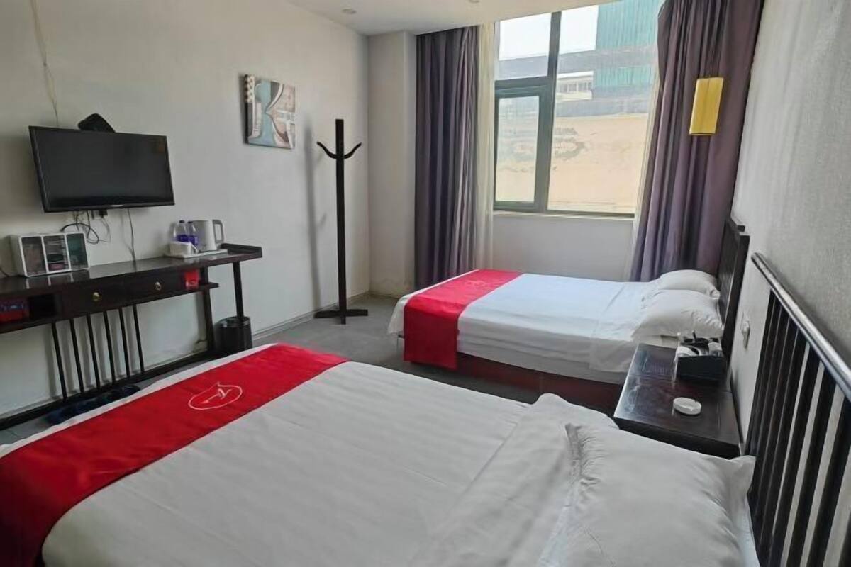 Une chambre d’hôtel avec deux lits, une télévision, un bureau avec un ordinateur et un téléphone, et une fenêtre avec des rideaux.
