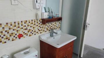 Un baño con salpicadero de azulejos, un lavabo blanco, un mueble de madera, un secador de pelo y un espejo.