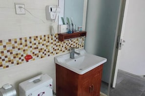 Casa de banho com painel de azulejos, pia branca, armário de madeira, secador de cabelo e espelho.