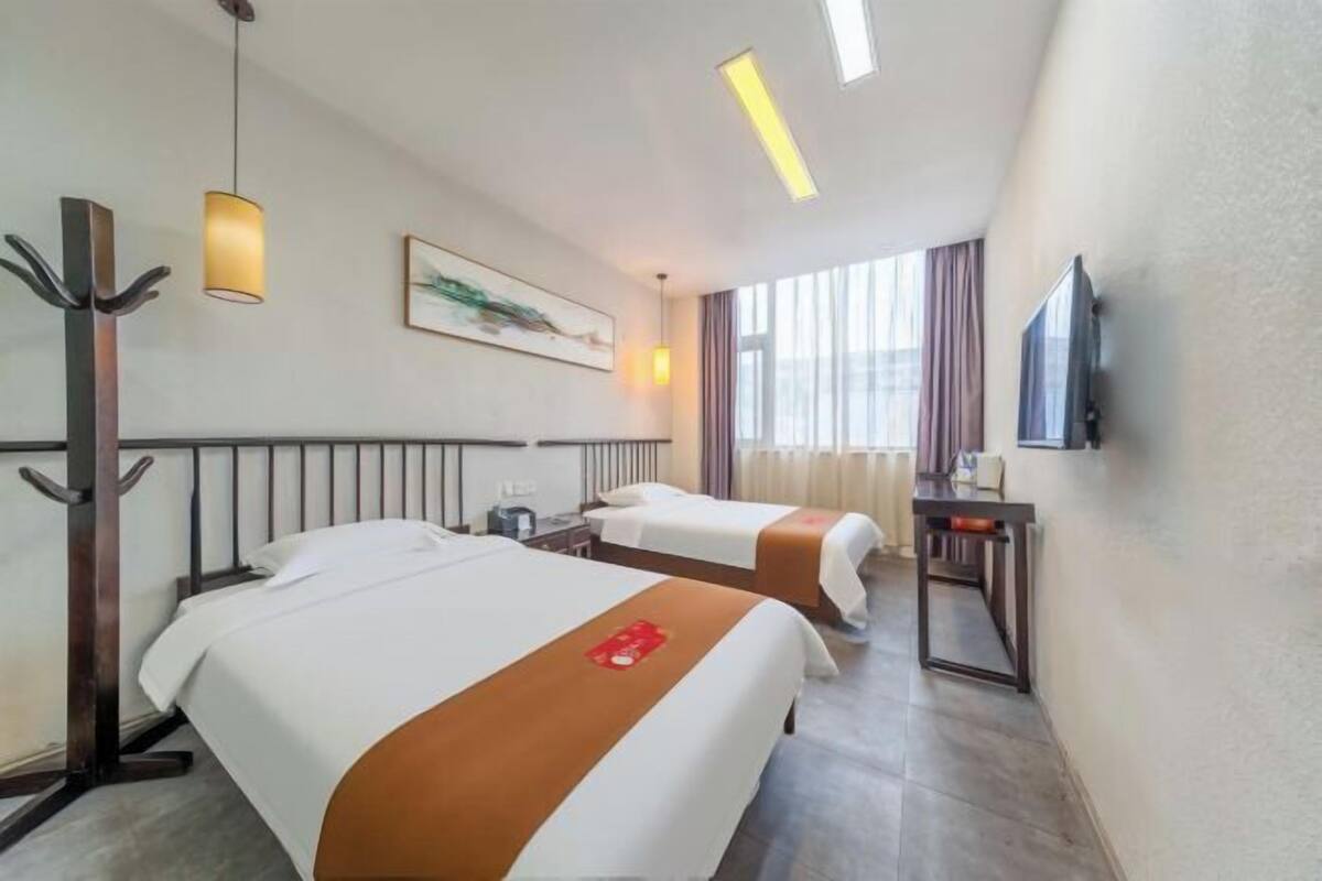 Une chambre d’hôtel avec deux lits, un bureau, une télévision et une fenêtre avec des rideaux.