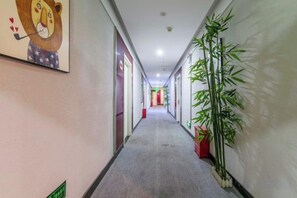 A hallway with a carpeted floor, a framed picture on the left, and potted plants on the right. - Yunshang Holiday Hotel (Zhengzhou Erqi Wanda Branch) (Zhengzhou)
