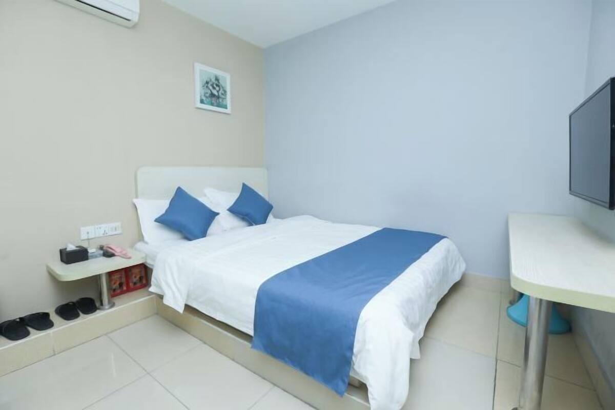 A hotel room with a bed, a bedside table, a TV, and a shoe rack.