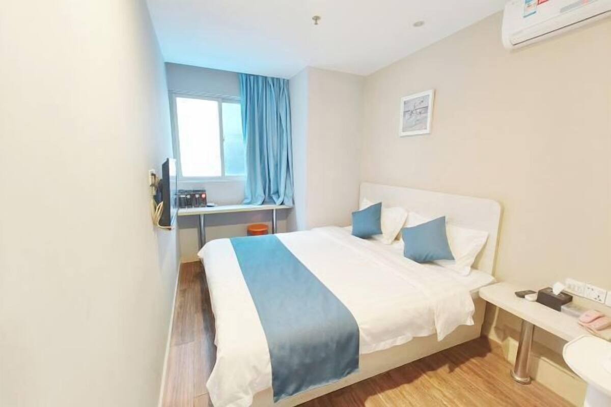 A hotel room with a bed, bedside table, and a window with curtains.