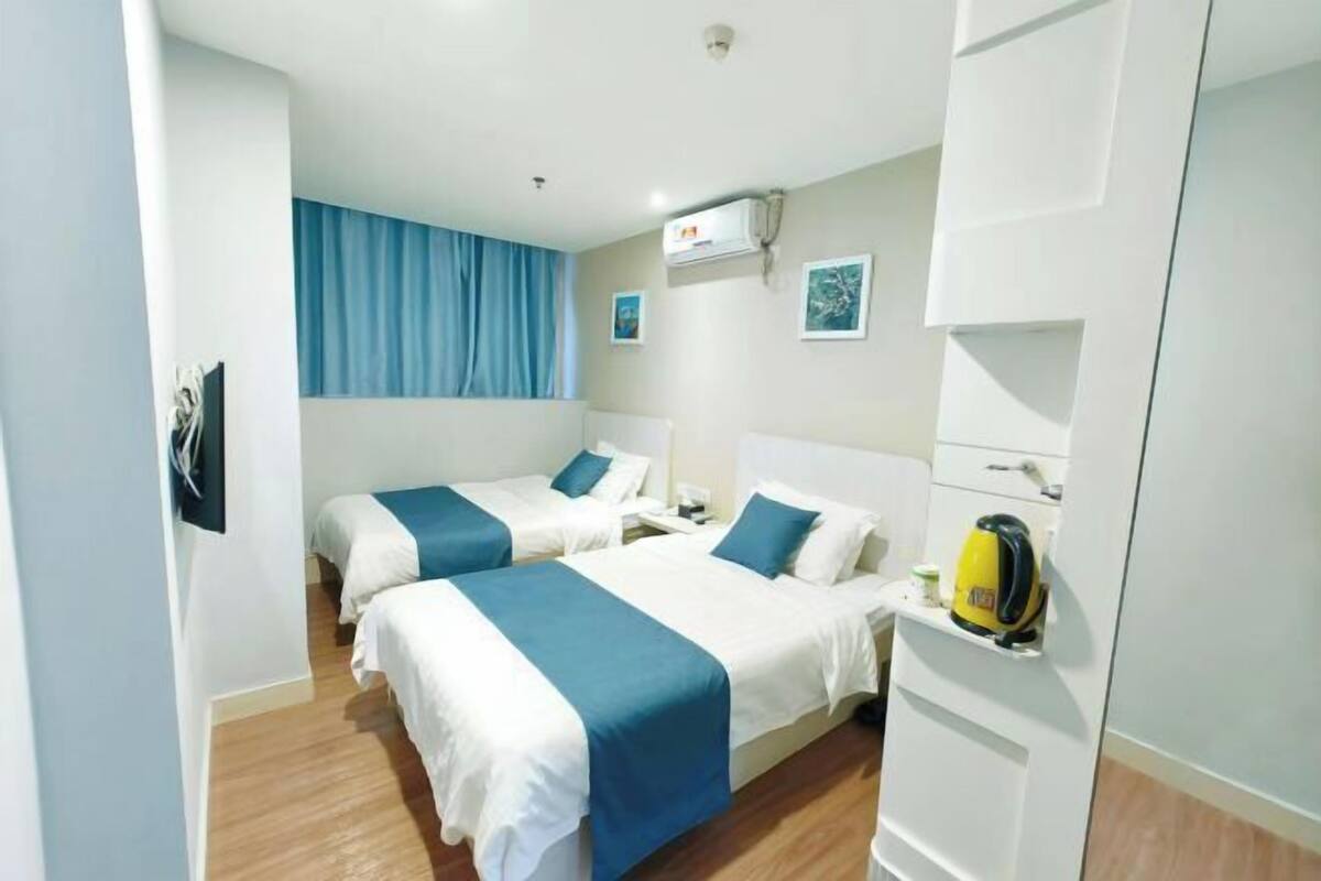 A hotel room with two beds, a wardrobe, a kettle, and a window with blue curtains.