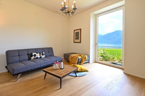 A living room with a sofa, a coffee table, and a view of a body of water through a large window. - Luxury Central Suite Garden in Lugano (Lugano)