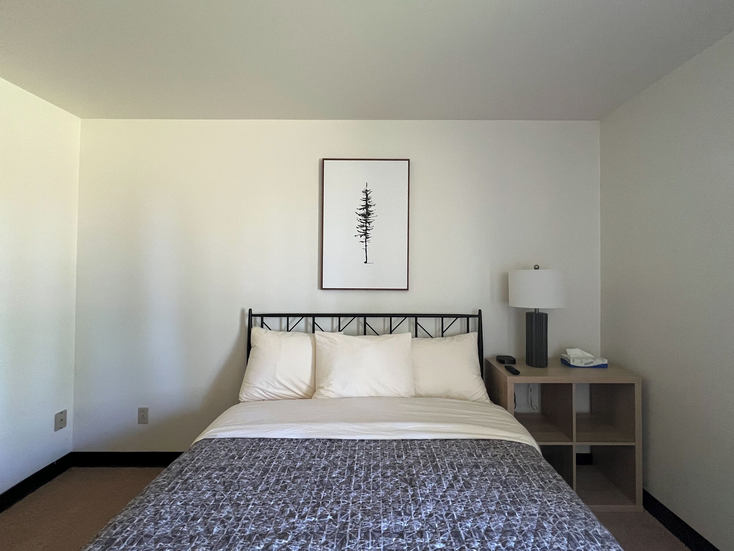 A hotel room with a bed, a bedside table with a lamp, and a framed picture on the wall.