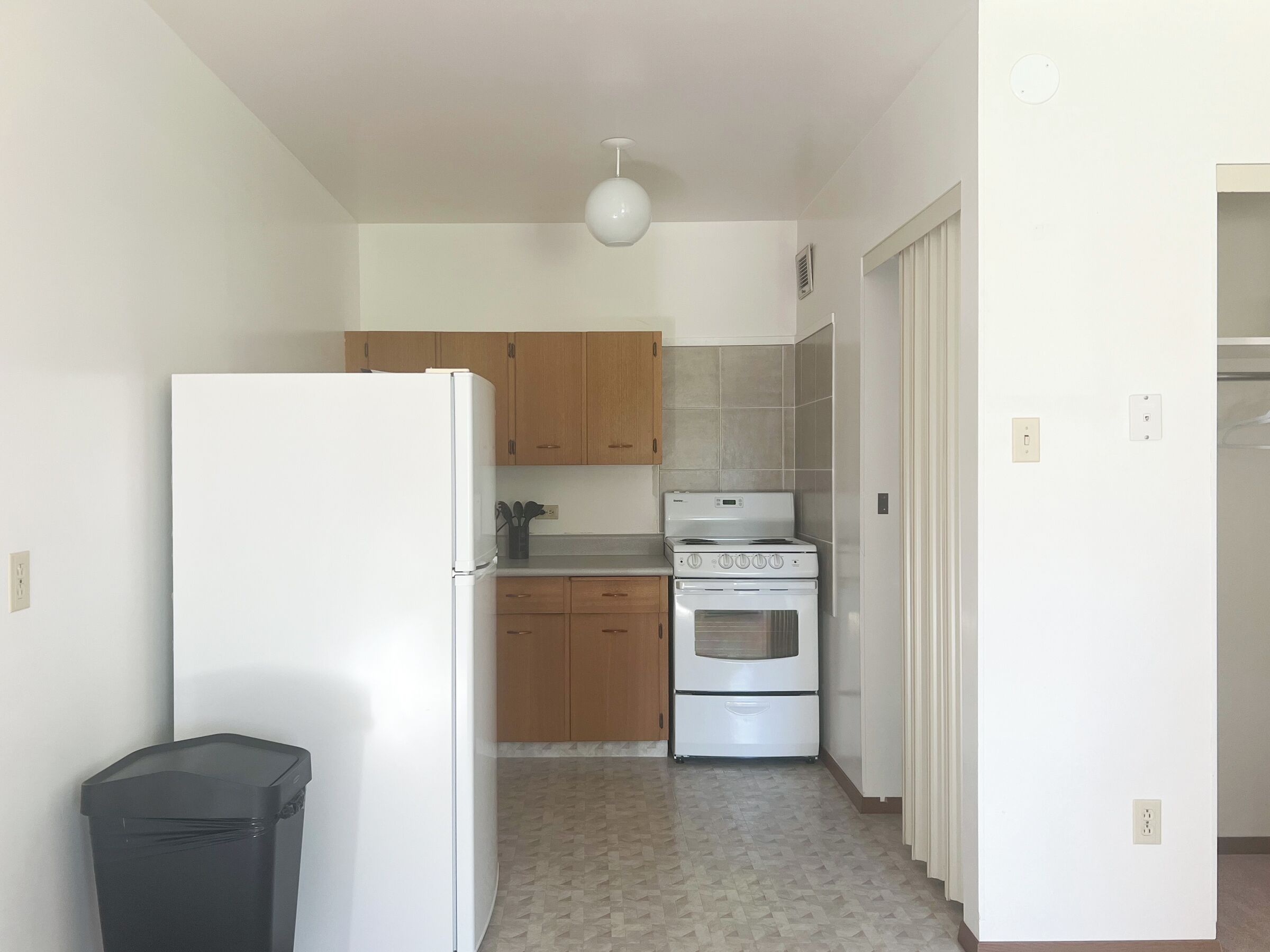 A compact kitchen with a refrigerator, stove, and wooden cabinets.