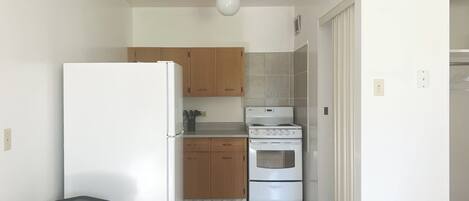A compact kitchen with a refrigerator, stove, and wooden cabinets.