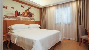 Quarto de hotel com uma cama grande, uma escrivaninha e uma cadeira. Há um mural na parede retratando instrumentos musicais e livros.