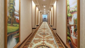 Corredor de hotel com piso estampado, paredes com obras de arte e teto com iluminação embutida.