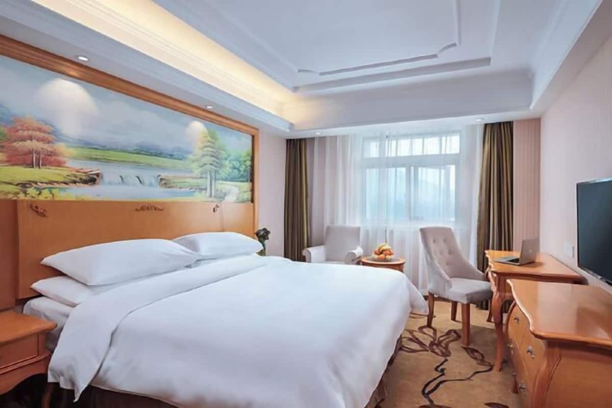 A hotel room with a large bed, a desk with a laptop, a chair, and a television.