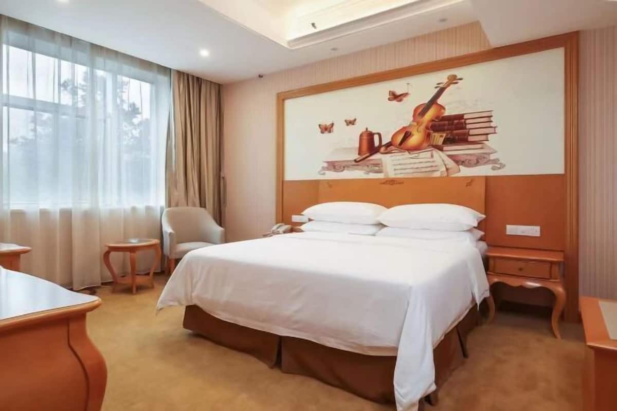 A hotel room with a large bed, a chair, a desk, and a painting on the wall.
